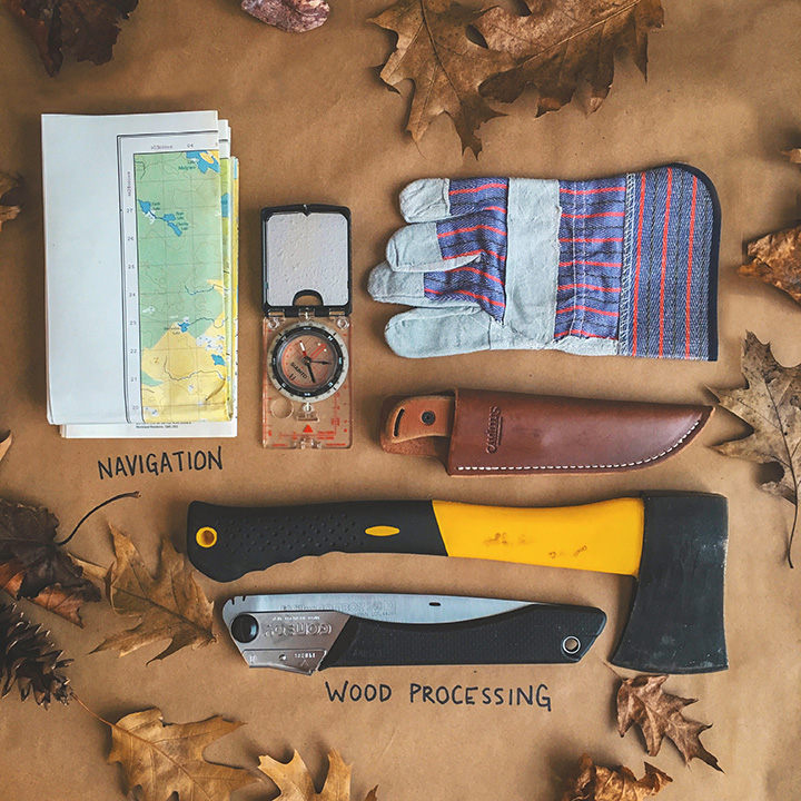 Flatlay of compass, axe, saw, map, knife, and gloves