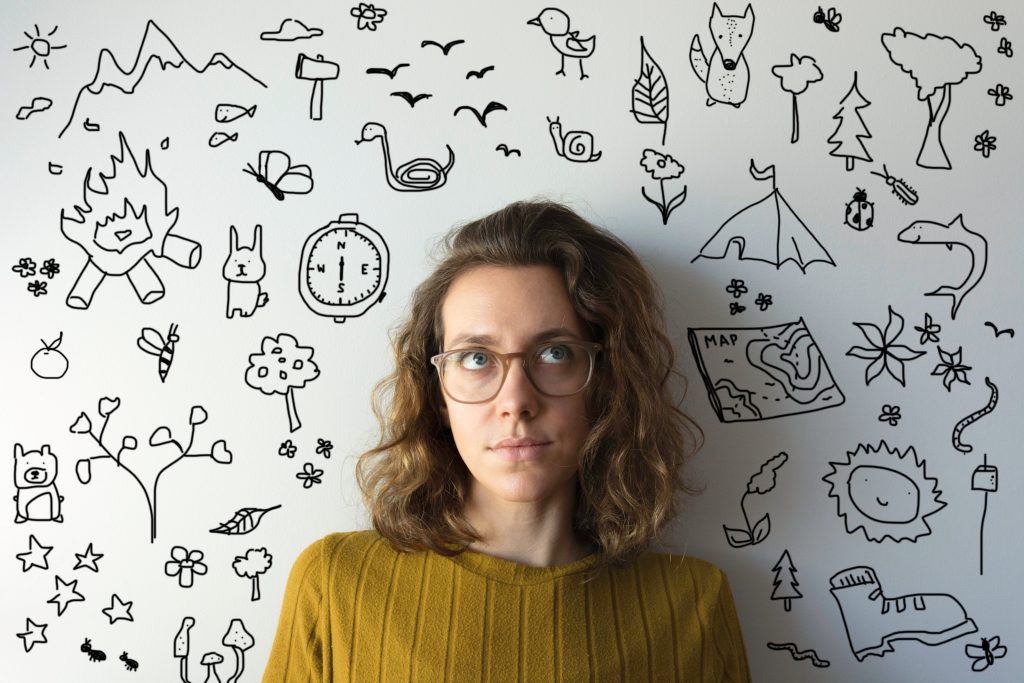Woman looks upwards imagining all the spring activities she wants to do. There are doodles of spring activities all around her (camping, map, compass, axe, mountains, flowers)