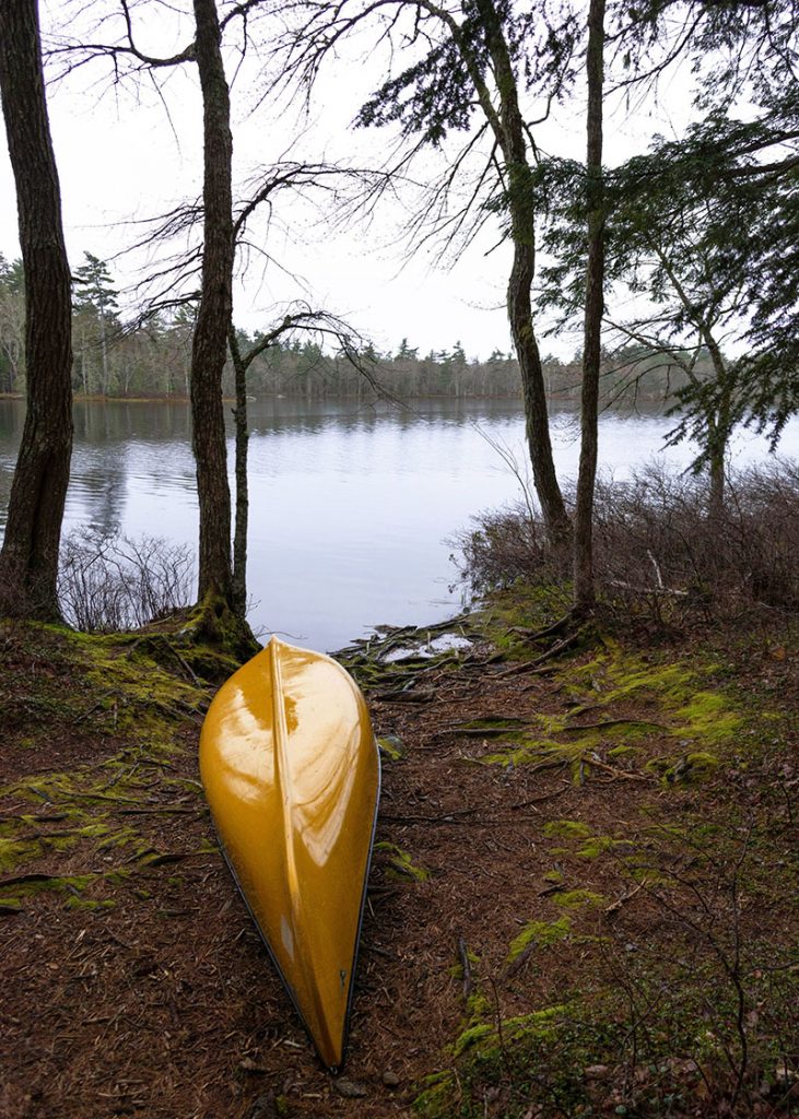 Yellow canoe is upside down on the shore. Frozen Lake is in the background.
